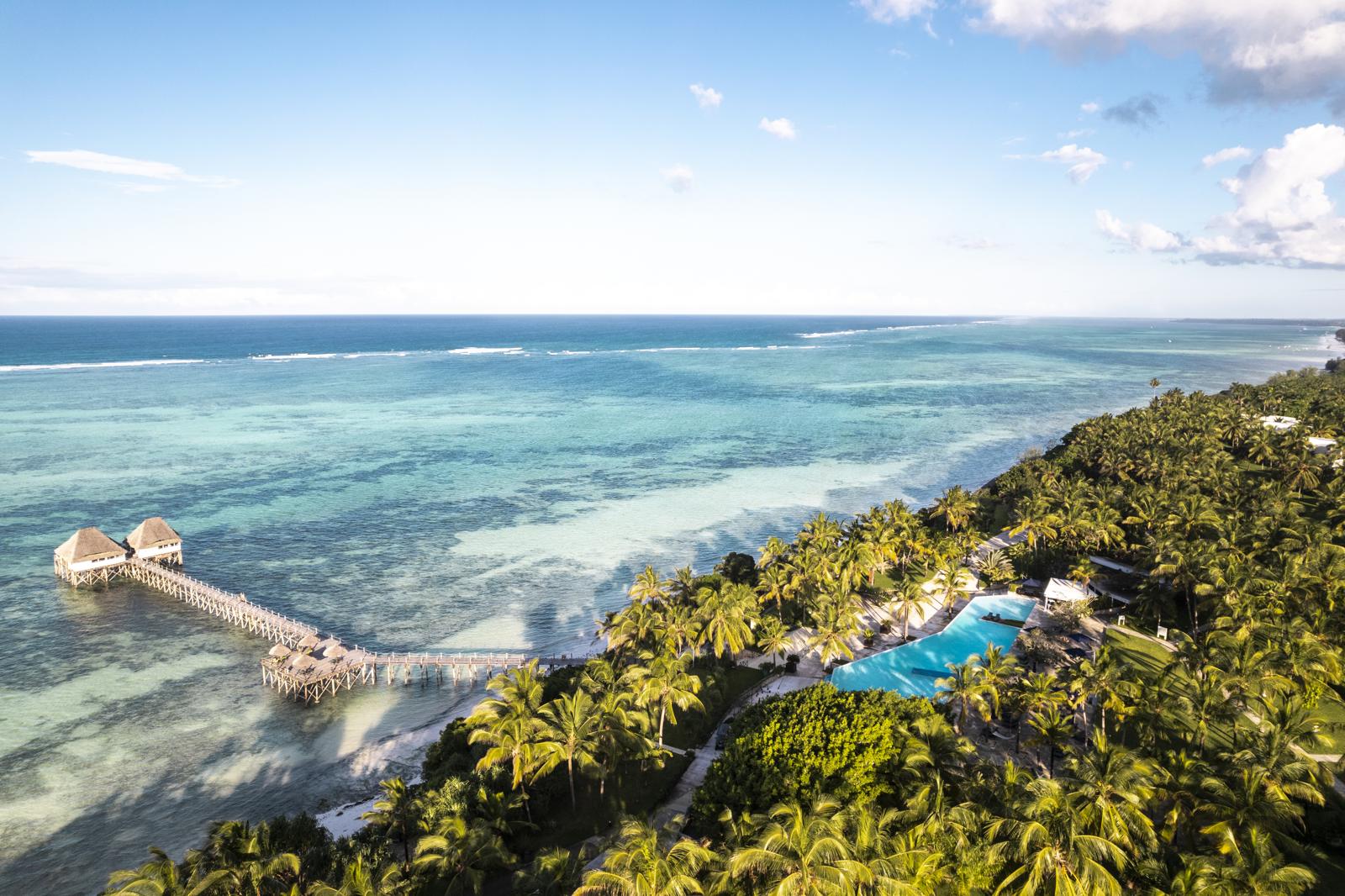 Vista aérea do resort entre coqueiros, com píer sobre o mar turquesa