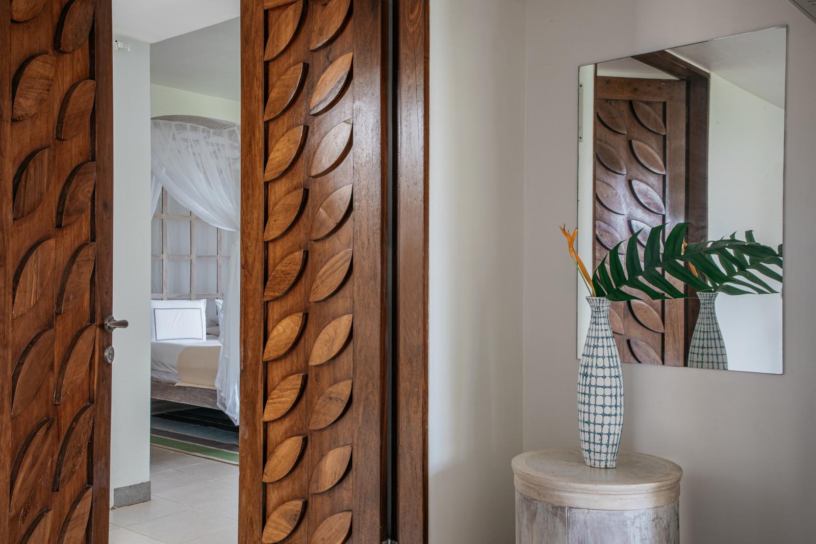 Porta de madeira com entalhes em forma de folhas, aberta para um quarto claro