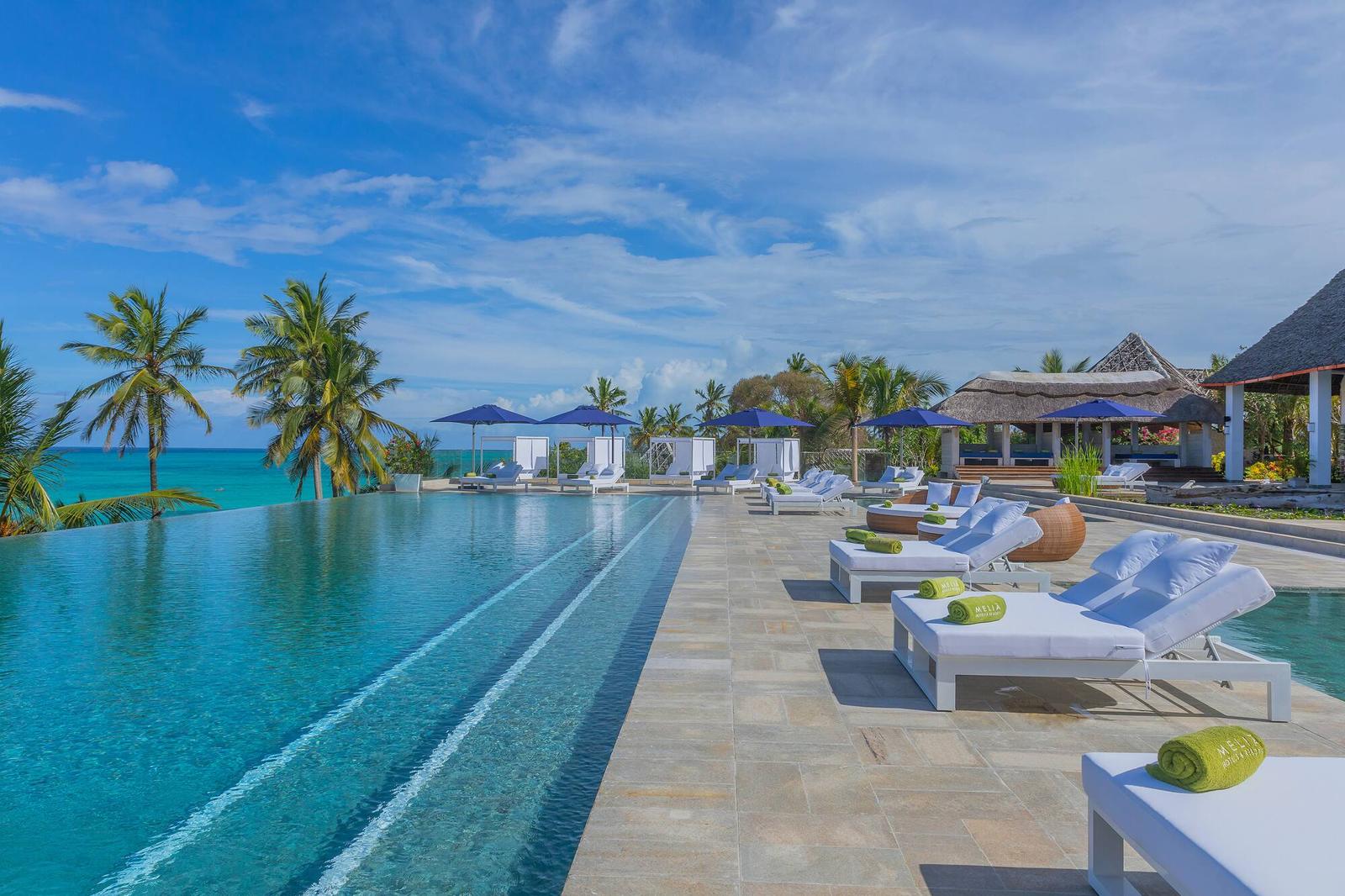 Piscina de borda infinita com espreguiçadeiras brancas e o mar ao fundo