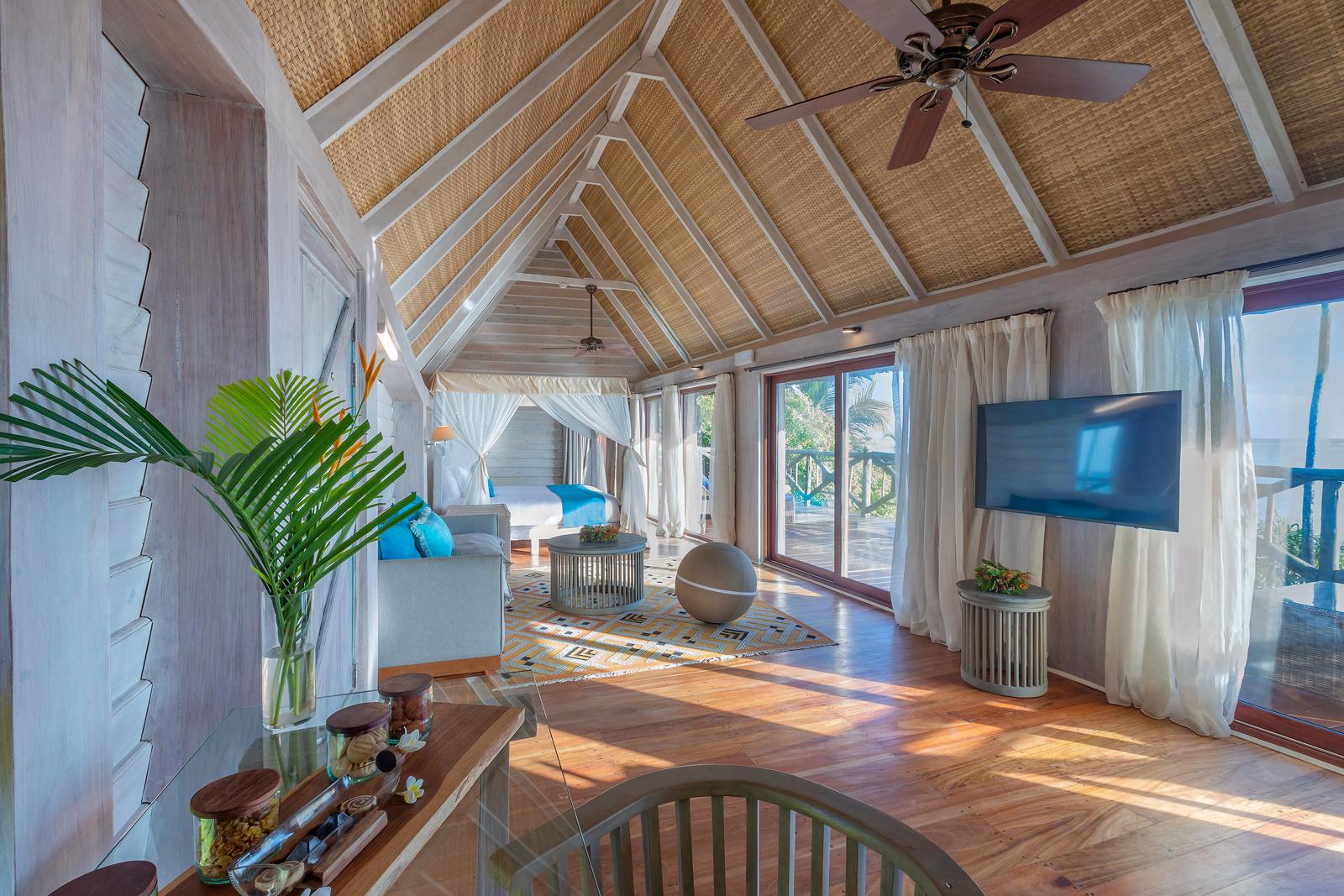Sala com forro alto de palha trançada, piso de madeira e vista para o mar
