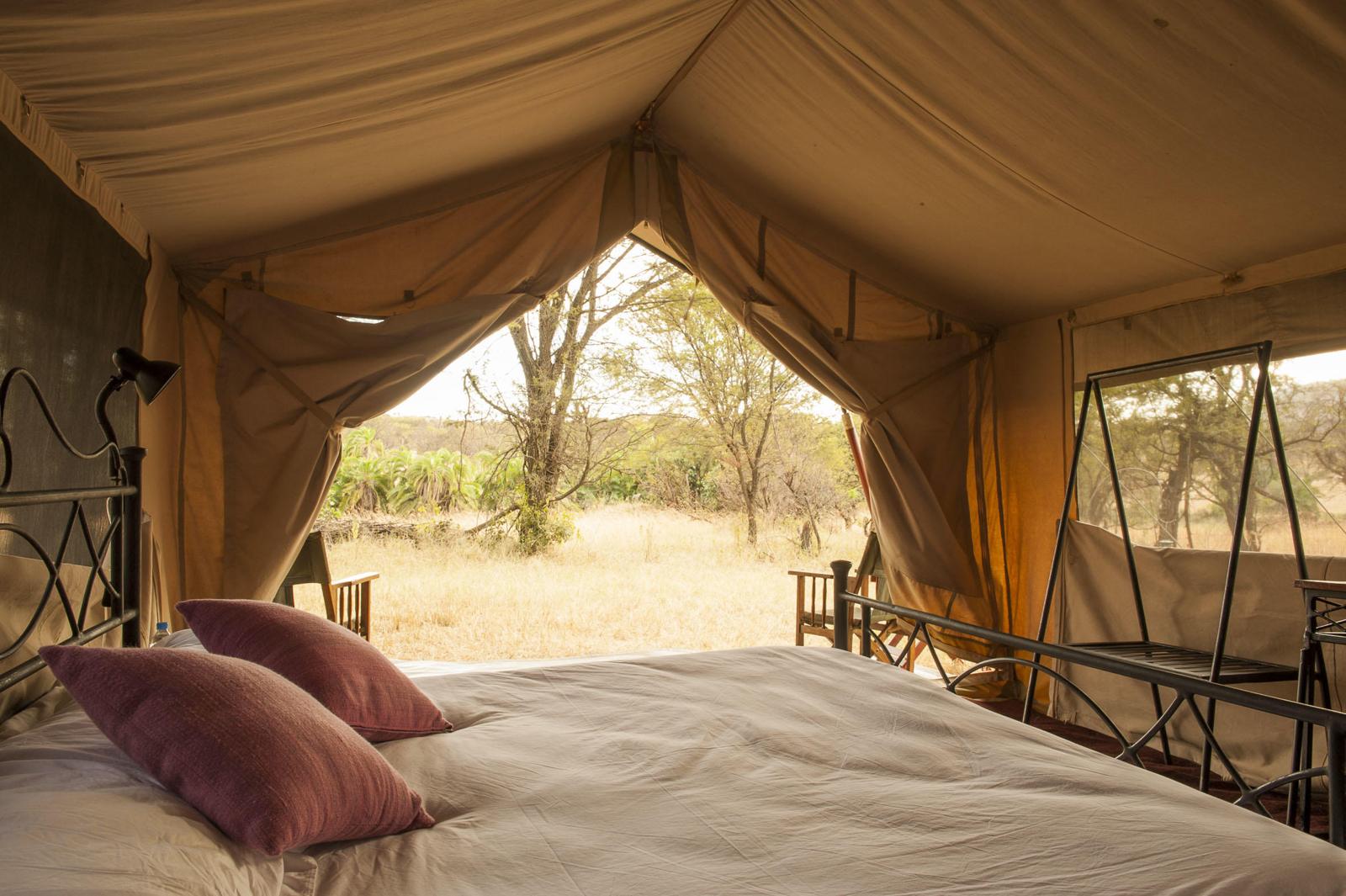 Cama voltada para a abertura da barraca, com vista para a savana