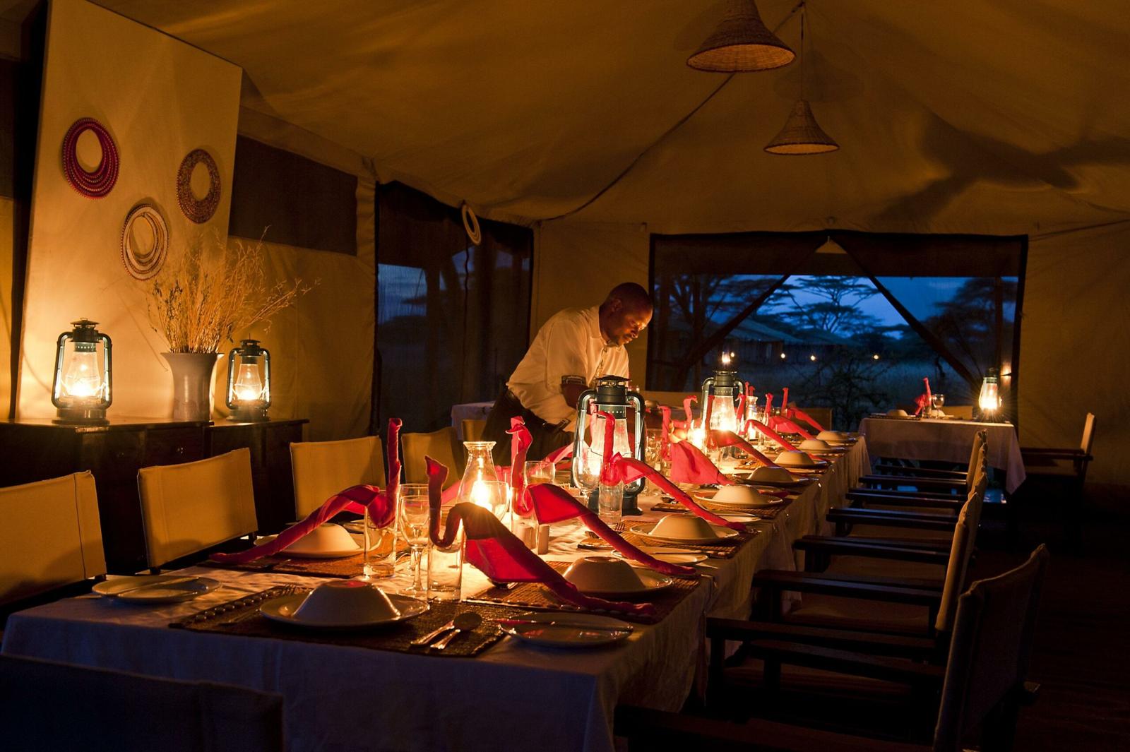 Mesa longa posta à luz de lanternas dentro da tenda-restaurante