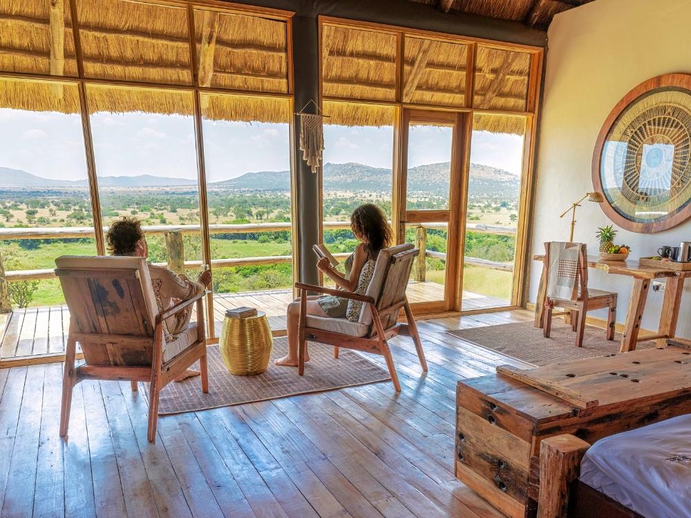 Sala do quarto com piso de madeira, poltronas e janelas abertas para a paisagem