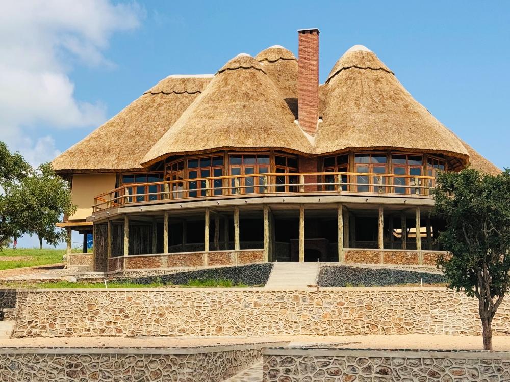 Edifício principal do lodge com telhados altos de palha e base de pedra