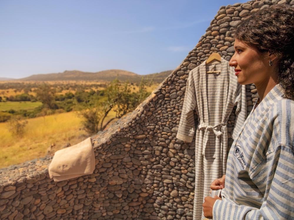 Parede curva de pedras arredondadas no chuveiro externo, com a savana ao fundo